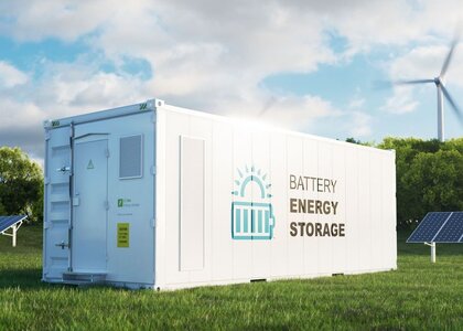 Image showing  a modern high-capacity battery energy storage systemIn a green field with solar panels in the background sits a large white container with the words “Batter energy storage” written on the side.