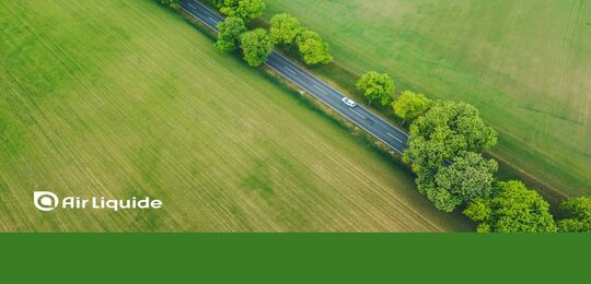 Image showing an arial view of a car driving down a road lined by trees and surrounded by green fields. Along the bottom is written “Air Liquide” and the company is credited for image on the left-hand side of the picture.