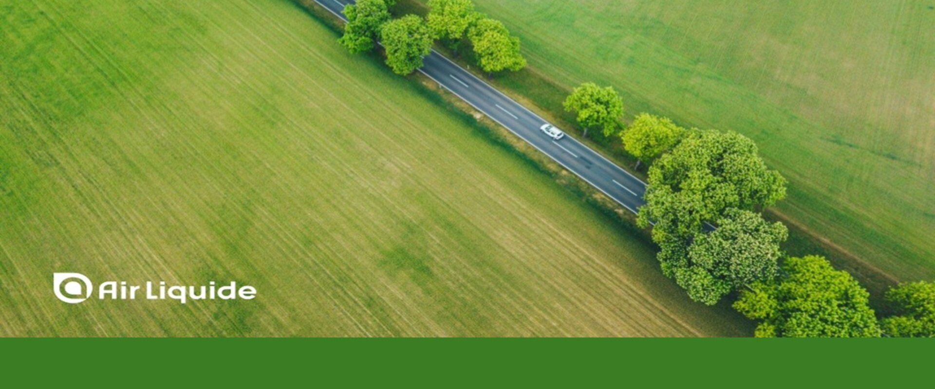 Image showing an arial view of a car driving down a road lined by trees and surrounded by green fields. Along the bottom is written “Air Liquide” and the company is credited for image on the left-hand side of the picture.
