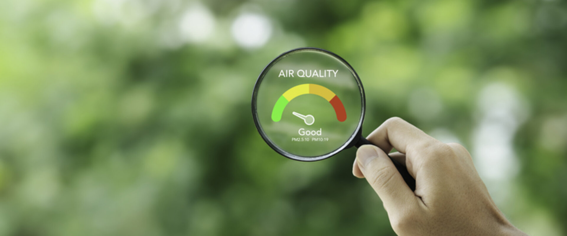Against a blurry background of trees, in the foreground is a hand holding a magnifying glass with the words “Air quality – Good” in its centre