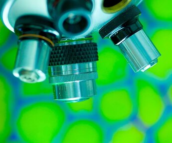 Close up of the lenses of a traditional microscope against a green background