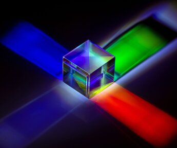Against a black background a glass cube gives out blue, green and red light from its sides