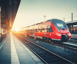 Railway station with beautiful modern red commuter train at sunrise Image showing a modern train pulling into a station at sunrise