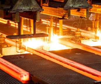 Hot steel bars on a conveyor belt inside a steel mill