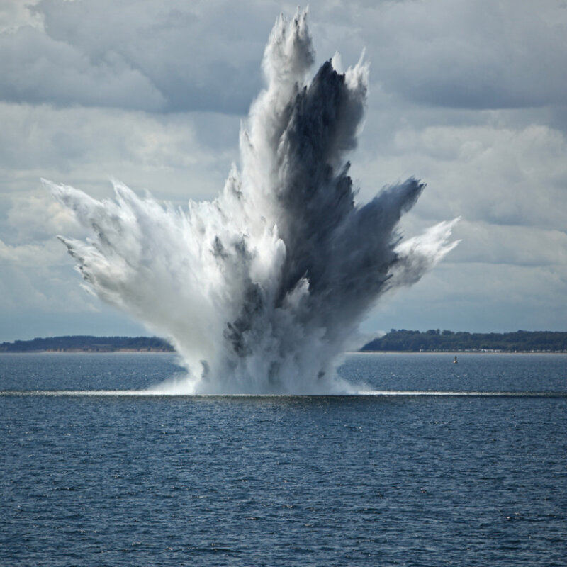 Providing traceability in low frequencies underwater, through the ground and the atmosphere Image showing a huge water fountain caused by a below surface explosion